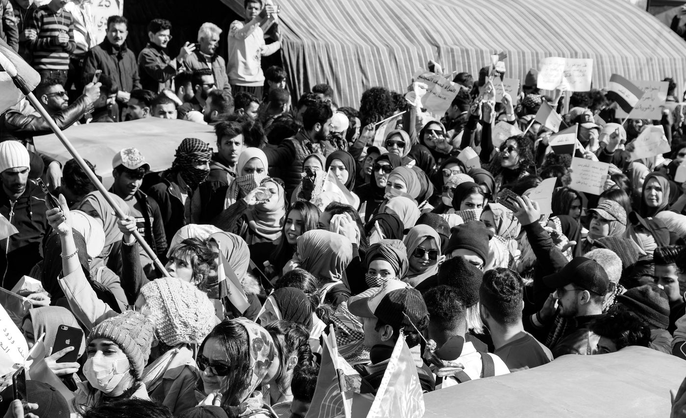 A dense crowd of women and men marching with flags and signs in Baghdad