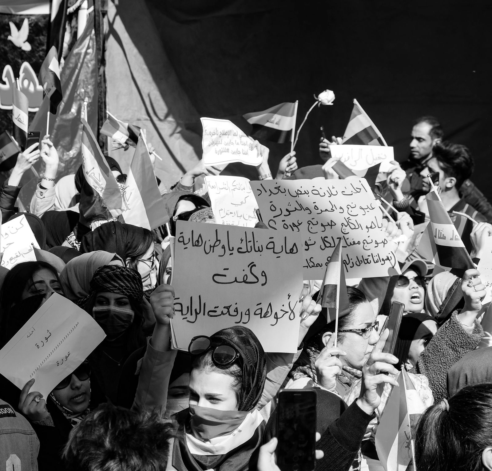 Women hold Iraqi flags and handwritten signs in a dense crowd at a march in Baghdad